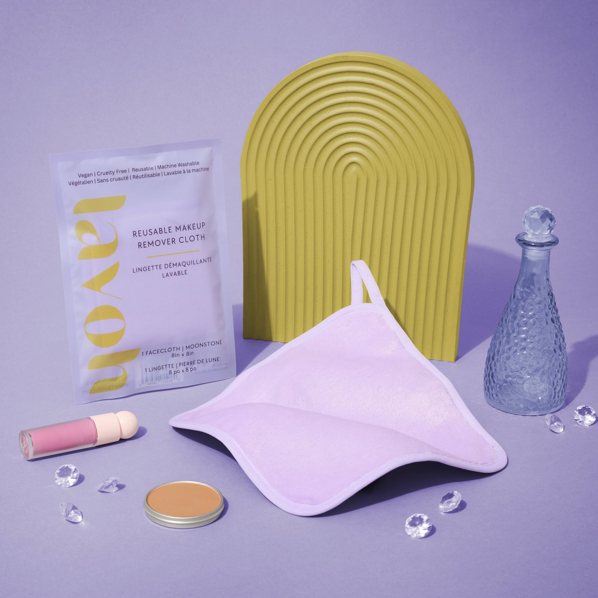 Makeup remover facecloth with a yellow arch, purple container, and various items on a purple background